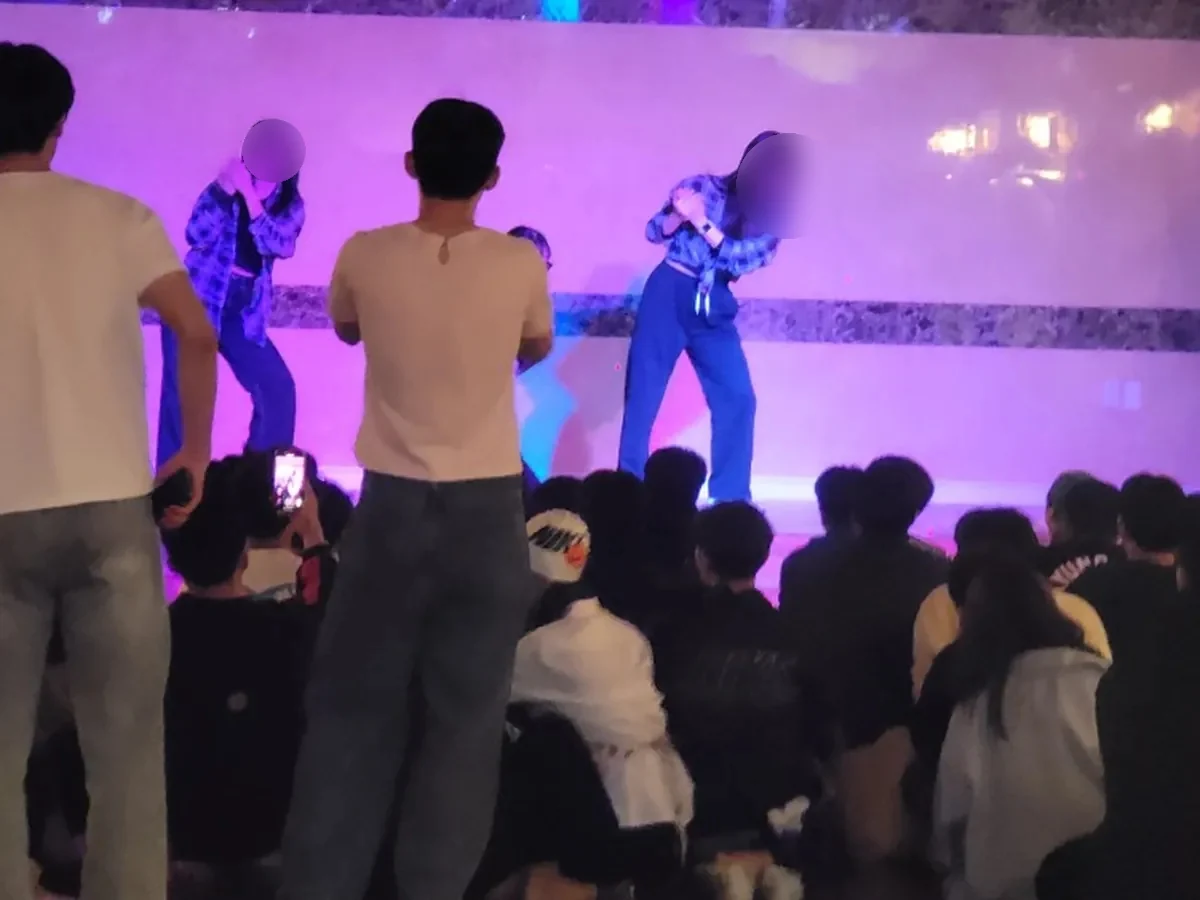 무대에서 노래하는 참가자와 둘러앉아 지켜보는 단체 인원