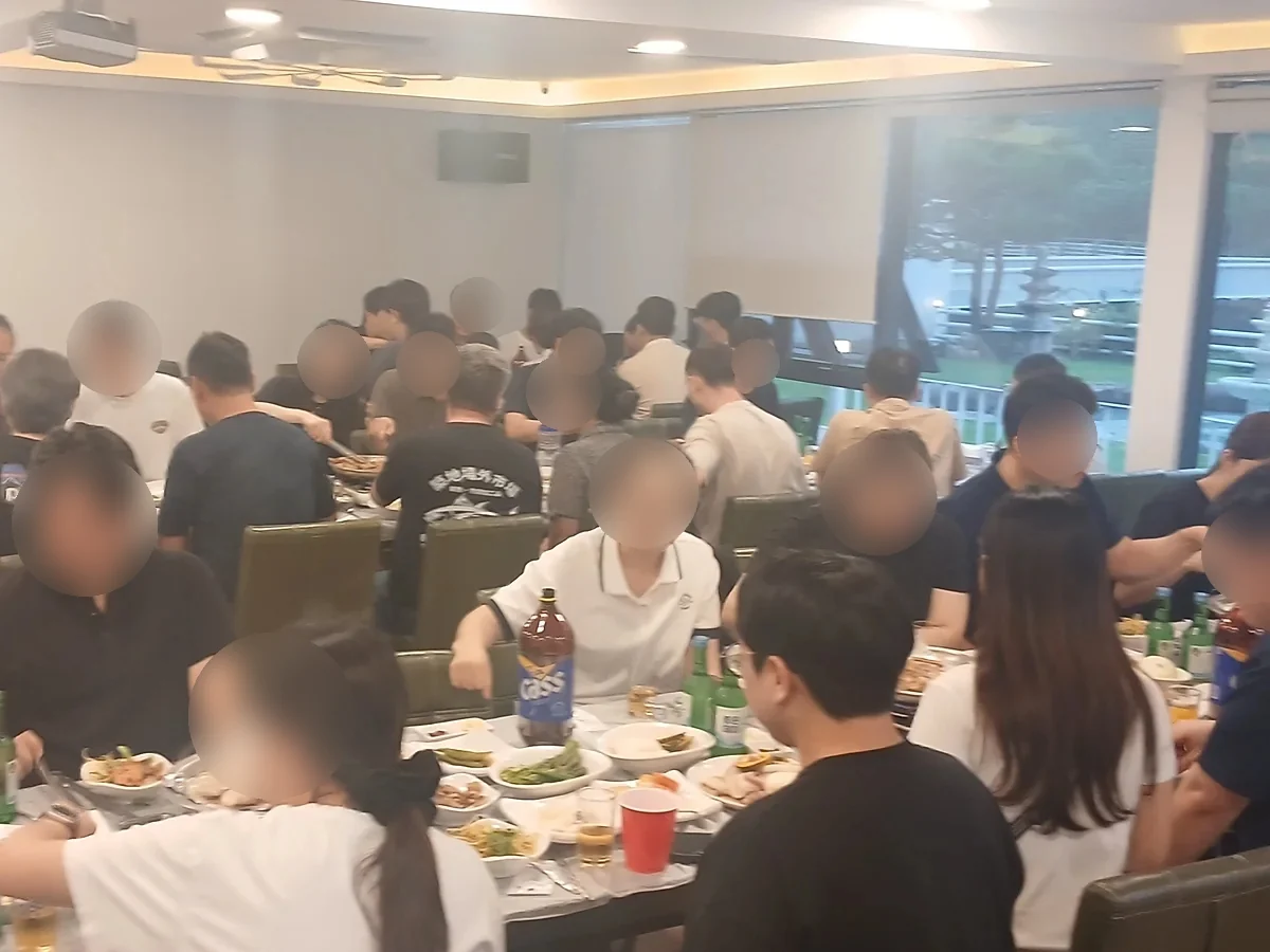 대형 홀에서 여럿이 둘러앉아 단체 식사를 하는 모습